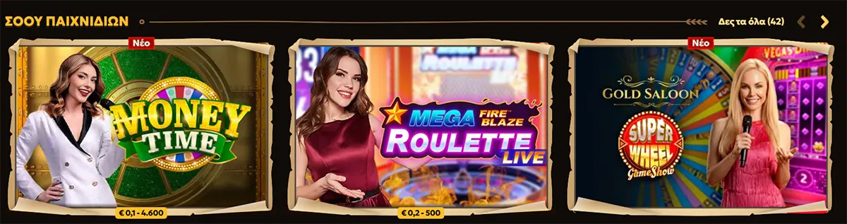 Greek live-casino section showing three game tiles: “Money Time” with a female host, “Mega Fire Blaze Roulette Live” with a female presenter, and “Gold Saloon Super Wheel Game Show” with a blonde host holding a microphone, with “Δες τα όλα (42)” in the top right.